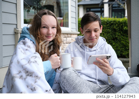 Teen boy with down syndrome pointing at laptop near friend with cup and cellphone two teenagers sit under a white blanket, boys, girls, drink tea, coffee on the porch, watch videos on a smartphone Teen boy with down syndrome pointing at laptop near friend with cup and cellphone two teenagers sit under a white blanket, boys, girls, drink tea, coffee on the porch, watch videos on a smartphone 114127943