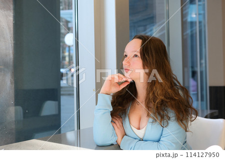 young beautiful teenage girl sits by the window in a cafe looks thoughtfully leaning on her arm look up raise her eyes dream thinking blue blouse woman growing up hormones beauty breast growth young beautiful teenage girl sits by the window in a cafe looks thoughtfully leaning on her arm look up raise her eyes dream thinking blue blouse woman growing up hormones beauty breast growth 114127950