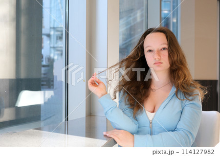 Close up picture of a young beautiful woman fixing her hair while looking at the camera. 114127982
