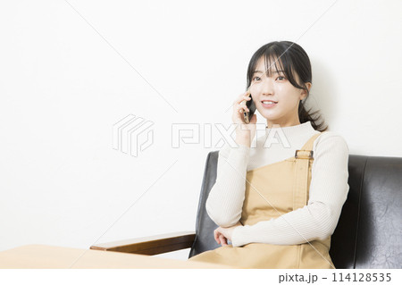ソファに座ってスマートフォンで通話する女性 ソファに座ってスマートフォンで通話する女性 114128535