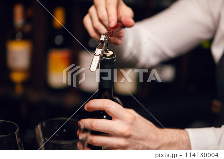 Bartender opening a wine bottle with corkscrew in restaurant with wine shelves. Bartender opening a wine bottle with corkscrew in restaurant with wine shelves. 114130004