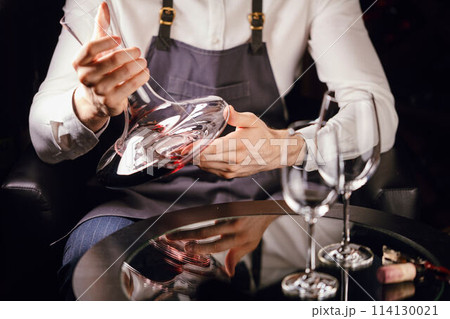 Skilled sommelier pouring wine from decanter ino wine glass. 114130021