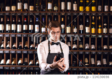 cavist or wine seller with a bottle of wine on the background of dark wine house cavist or wine seller with a bottle of wine on the background of dark wine house 114130036