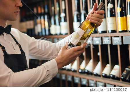 cavist or wine seller with a bottle of wine on the background of dark wine house cavist or wine seller with a bottle of wine on the background of dark wine house 114130037