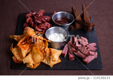 Top view of a plate of food with bread, meat, sausage, and chips with dip. 114130215