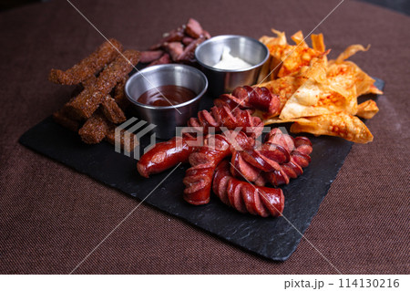 Top view of a plate of food with bread, meat, sausage, and chips with dip. 114130216
