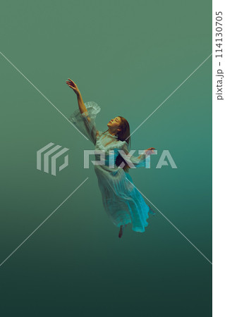 Reach for light. Woman in flowing white vintage gown reaches upwards to sky from dark teal depth of ocean waters. 114130705