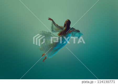 Woman in stunning dress, gracefully suspend in mid-air, conveys sense of fluidity and grace against serene aqua background. Woman in stunning dress, gracefully suspend in mid-air, conveys sense of fluidity and grace against serene aqua background. 114130771