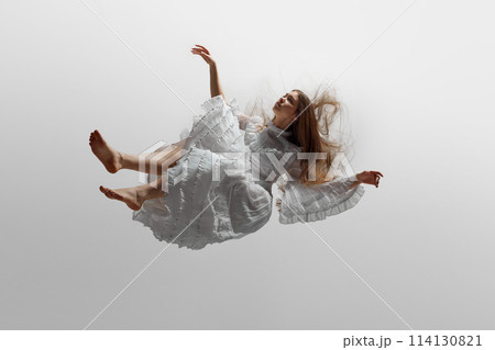 Young woman, dressed in elegant white dress with delicate ruffles, seems to levitate against white studio background. Young woman, dressed in elegant white dress with delicate ruffles, seems to levitate against white studio background. 114130821
