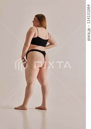 Power of self-care and positive body image. Full-length of young girl with oversized body standing in underwear against grey studio background 114131064