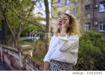 middle age woman in 70s, 80s style clothes with a coffee stain on her blouse in front of gray houses of the 70s 114132261