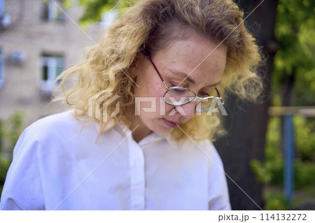 middle age woman in 70s, 80s style clothes with a coffee stain on her blouse in front of gray houses of the 70s 114132272