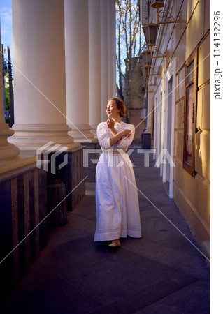 elegant middle age woman in white vintage dress near theater with antique colonnades 114132296
