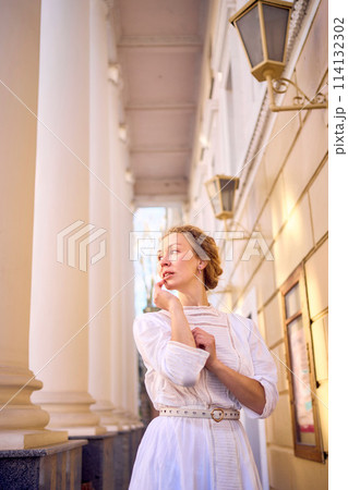 elegant middle age woman in white vintage dress near theater with antique colonnades 114132302