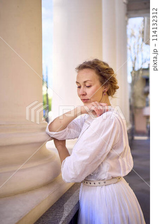 elegant middle age woman in white vintage dress near theater with antique colonnades 114132312