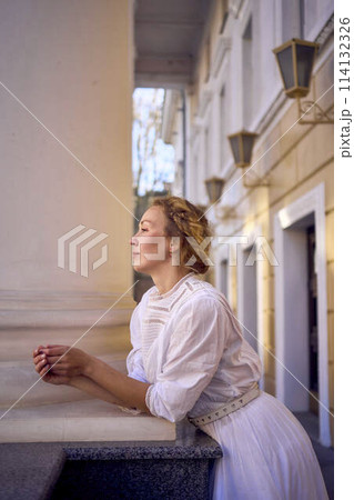 elegant middle age woman in white vintage dress near theater with antique colonnades 114132326
