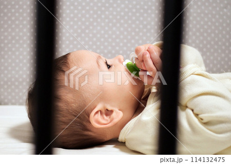 Baby sucking Pacifier looking on bed. portrait of cute newborn baby lying on bed with pacifier on mouth Baby sucking Pacifier looking on bed. portrait of cute newborn baby lying on bed with pacifier on mouth 114132475