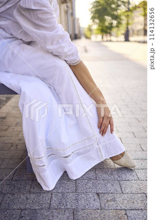 elegant middle age woman in a white vintage dress sitting on a bench in the morning city 114132656