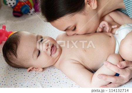 Young mother, kissing her baby boy at home. Family concept. Closeup portrait of loving mother young woman kissing little kid, home interior 114132714