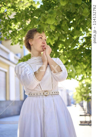 elegant middle age woman in a white vintage dress against the background of historical buildings in the morning light 114132762