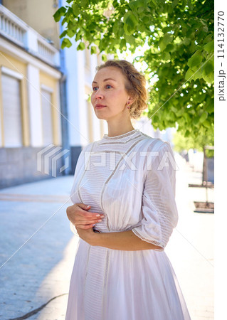 elegant middle age woman in a white vintage dress against the background of historical buildings in the morning light 114132770