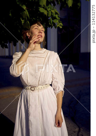 elegant middle age woman in a white vintage dress against the background of historical buildings in the morning light elegant middle age woman in a white vintage dress against the background of historical buildings in the morning light 114132775