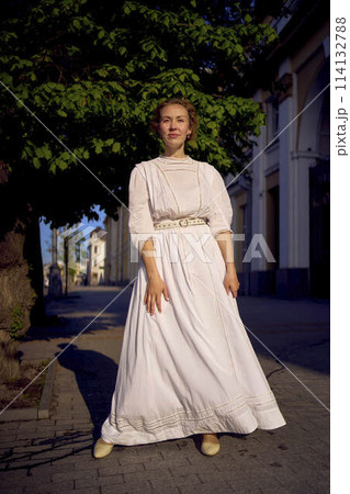 elegant middle age woman in a white vintage dress against the background of historical buildings in the morning light 114132788