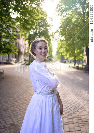 chic middle age woman in a white vintage dress in a sunlit alley 114132809