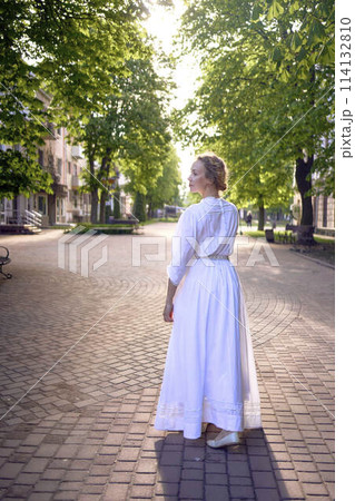 chic middle age woman in a white vintage dress in a sunlit alley 114132810