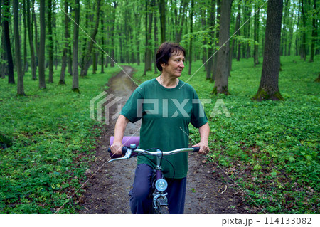 elderly woman walking in spring forest with bicycle and yoga mat 114133082