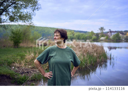 old woman doing exercises in the morning on the river bank, a bicycle and a yogamat next to her 114133116