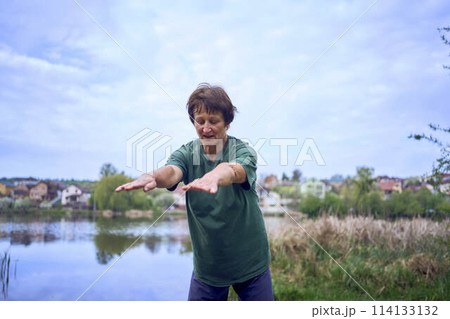 old woman doing exercises in the morning on the river bank, a bicycle and a yogamat next to her 114133132