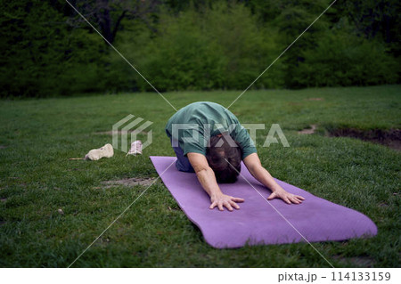 old woman practices yoga in the morning on the river bank, came from home by bicycle 114133159