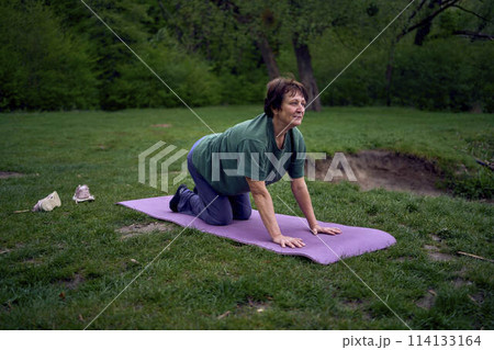 old woman practices yoga in the morning on the river bank, came from home by bicycle old woman practices yoga in the morning on the river bank, came from home by bicycle 114133164