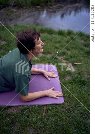 old woman practices yoga in the morning on the river bank, came from home by bicycle 114133208