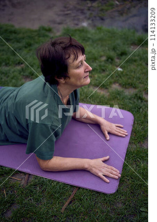 old woman practices yoga in the morning on the river bank, came from home by bicycle old woman practices yoga in the morning on the river bank, came from home by bicycle 114133209