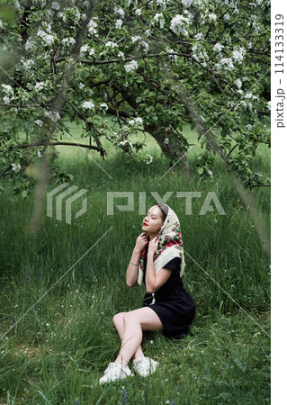 Slavic girl in a scarf near blooming apple trees 114133319