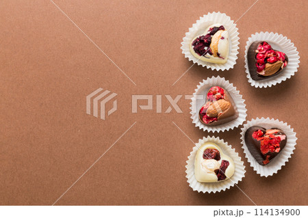chocolate sweets in the form of a heart with fruits and nuts on a colored background. top view with space for text, holiday concept chocolate sweets in the form of a heart with fruits and nuts on a colored background. top view with space for text, holiday concept 114134900