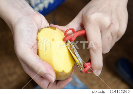 Woman peels potatoes while sitting on a chair in the kitchen Woman peels potatoes while sitting on a chair in the kitchen 114135260