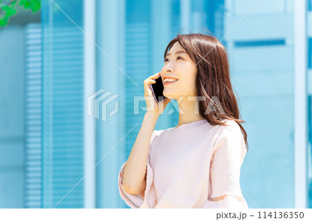 屋外でスマホを使って話す笑顔のビジネスウーマン 屋外でスマホを使って話す笑顔のビジネスウーマン 114136350