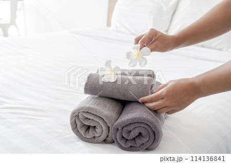 Hands of hotel maid putting plumeria flower and towels on the bed in the luxury hotel room ready for tourist travel Hands of hotel maid putting plumeria flower and towels on the bed in the luxury hotel room ready for tourist travel 114136841