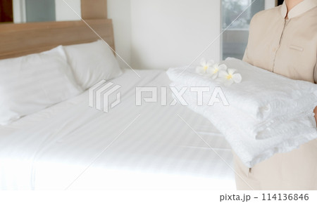 Hands of hotel maid putting plumeria flower and towels on the bed in the luxury hotel room ready for tourist travel Hands of hotel maid putting plumeria flower and towels on the bed in the luxury hotel room ready for tourist travel 114136846