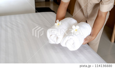 Hands of hotel maid putting plumeria flower and towels on the bed in the luxury hotel room ready for tourist travel 114136880