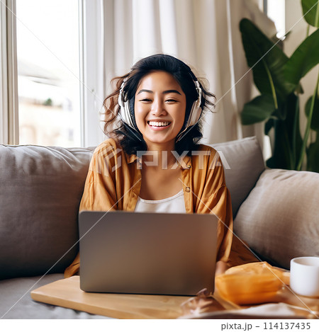 Asian Woman Embracing Relaxation, Lounging on Couch with Laptop and Podcast 114137435