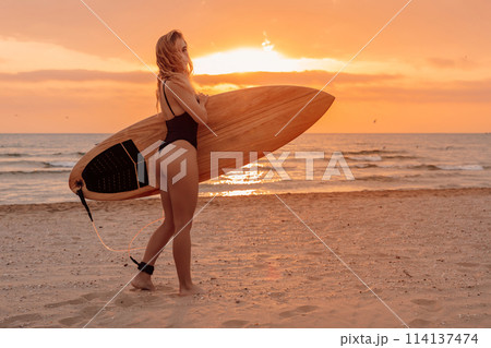 Surfgirl with long hair go to surfing. Woman holding surfboard on a beach at sunset or sunrise. Surfer and ocean 114137474