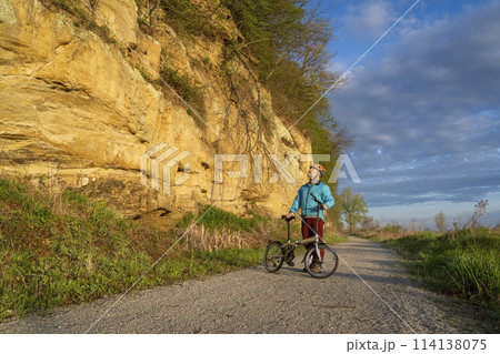 senior male cyclist riding a folding bike on Steamboat Trace, bike trail converted from an abandoned railroad, near Peru, Nebraska, springtime morning scenery 114138075
