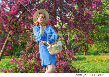young woman in park enjoying a picnic. She holds an iron basket with fruits 114139050
