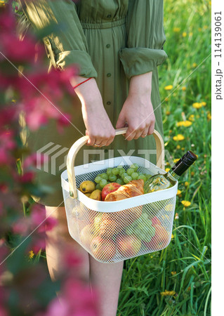young woman in park, enjoying picnic. She holds metal picnic basket 114139061