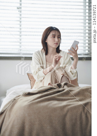 ベッドでスマートフォンを見る20代女性 114139721