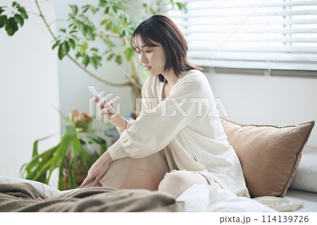 ベッドでスマートフォンを見る20代女性 114139726